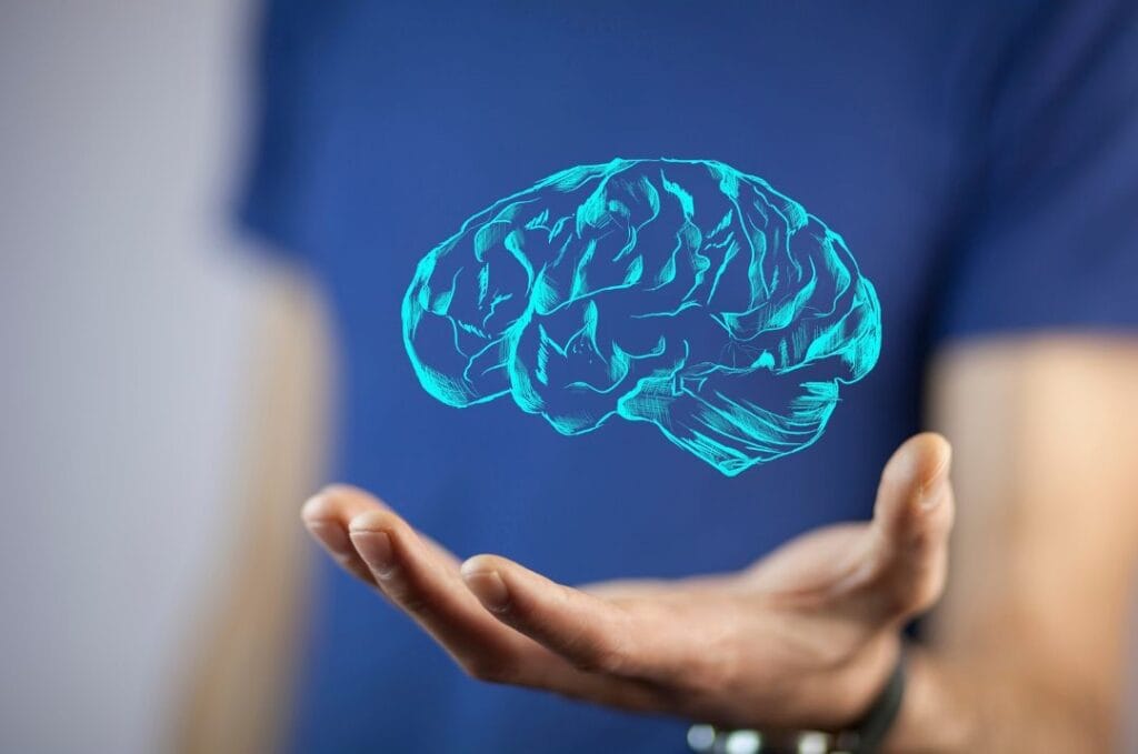 A person holds out their hand with a digital hologram of a brain projected above it, illustrating the future of clinicians online as they integrate technology into psychotherapy sessions.