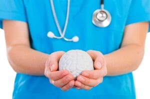 A person in blue scrubs, emblematic of a mental health clinic, holds a model of a brain with a stethoscope draped around their neck. hypnotherapy
